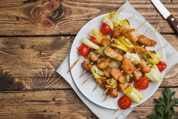 Kebab chicken, zucchini and tomatoes on skewers in a plate. Wooden table. Copy space