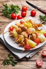Kebab chicken, zucchini and tomatoes on skewers in a plate. Wooden table.