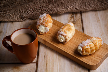 Cream cakes on a wooden plate with a cup of coffee with milk. The concept of natural and delicious food.