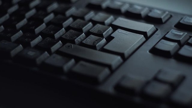 Close-up man presses keyboard key. Man presses button enter computer keyboard. Man's hand presses keyboard in light of computer screen