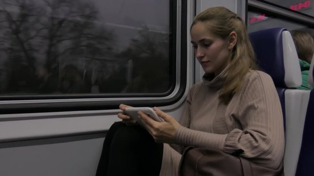 Beautiful young woman holding white tablet traveling by train 