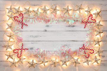 A border of golden star christmas lights, tinsel and candy sticks, on a destressed woodern background