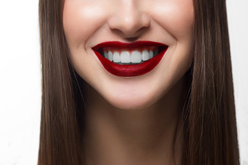 Fototapeta premium Close-up shot of sexy woman lips with red lipstick and white teeth. Perfect clean skin, fashion lip make-up. Beautiful spa portrait with tender pink flower. Spa and cosmetics