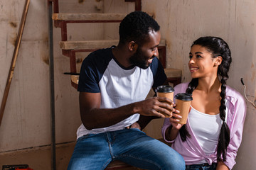 young african american couple clinking by disposable cups of coffee during renovation at new home