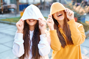 two young girls walking city having fun. joyful Women in bright colored hoodies walking, laughing...