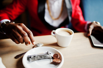 Fototapeta na wymiar Hands of fashion african american man model at red suit, sitting at cafe with coffee.