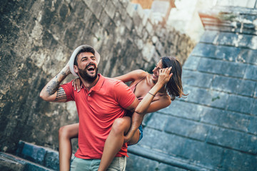 Traveling couple of tourists walking around old town. Vacation, summer, holiday, tourism: concept. Man giving a piggyback ride to his girlfriend.