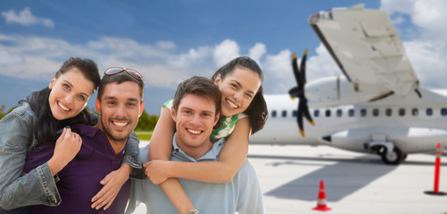tourism, travel and people concept - group of happy friends over plane on airfield background