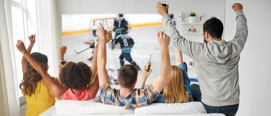 friendship, sport and leisure concept - happy friends drinking beer and watching ice hockey game on...