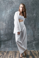 Fashion shot of brunette woman posing in white shirt, top and pants. Studio, grey background