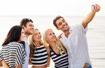 friendship, summer holidays and people concept - group of happy friends taking picture by smartphone on beach