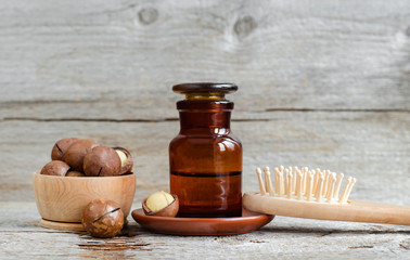 Obraz na płótnie Canvas Pharmacy bottle with macadamia nut oil and wooden hair brush. Ingredients of homemade cosmetics - face and hair masks and moisturizers. Wooden background. Copy space. 