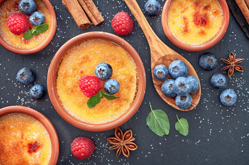 Creme brulee (cream brulee, burnt cream) with raspberry, blueberry and mint in terracota clay baking dishes