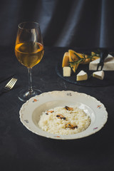 risotto with mussels (seafood rice) in a white plate and a glass of white wine on a dark background