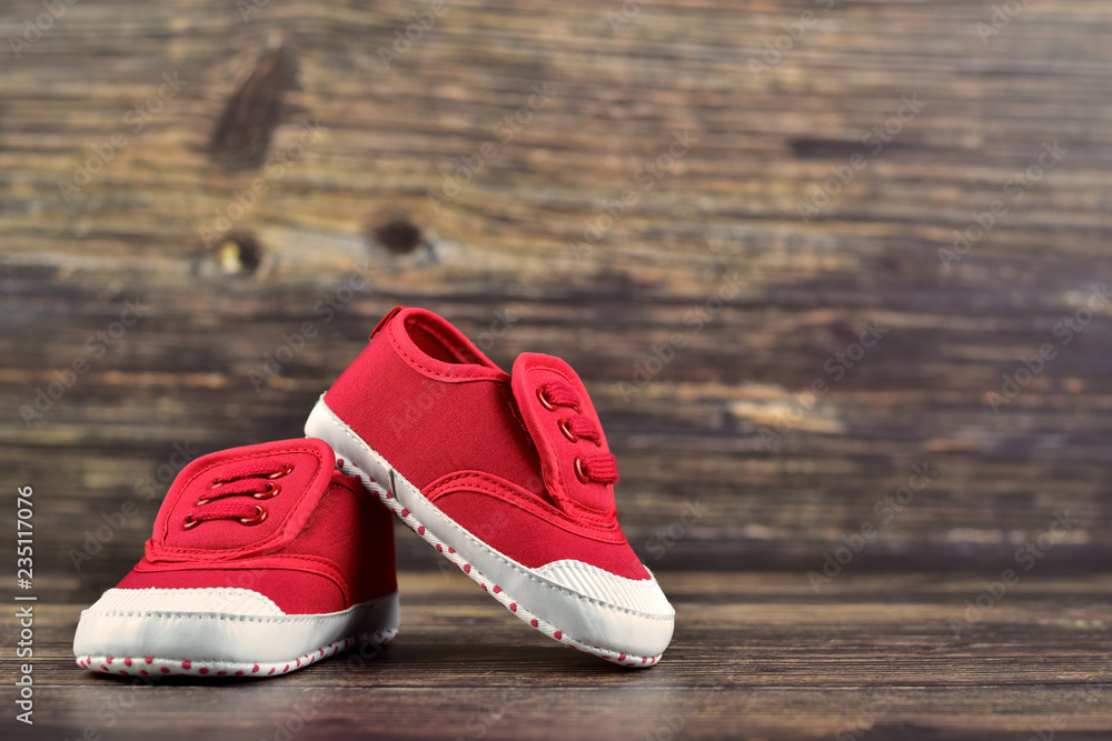 Wall mural a pair of red baby boy shoes/sneakers on dark wooden background, kid's clothes concept, traveling wi