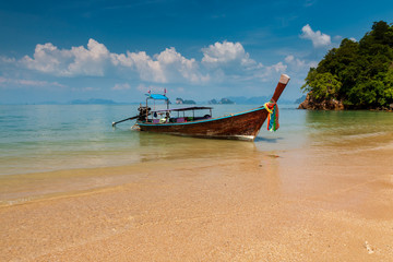 A traditional Longtail boat anchored next to a beautiful sandy beach on an island in Thailand