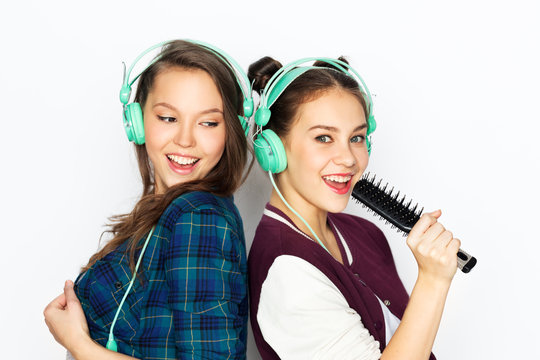 people, leisure and technology concept - smiling teenage girls in earphones listening to music and singing to hairbrush and having fun over white background