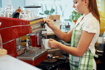 Side view of pretty barista woman in apron making coffee with machine standing at counter in coffee shop