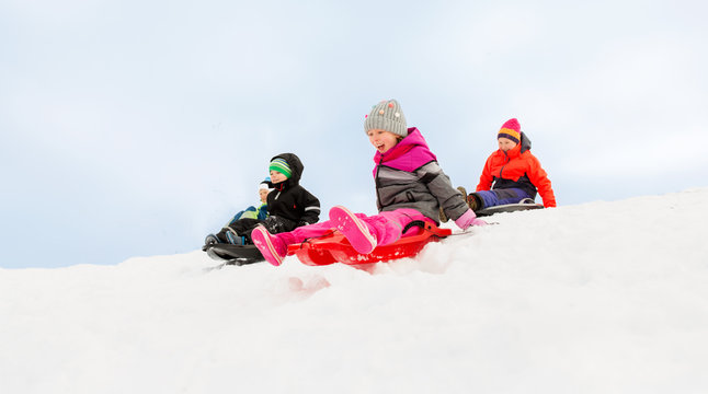 childhood, sledging and season concept - group of happy little kids sliding on sleds down snow hill in winter