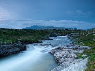 River with hills and rocks in cloudy weather, Rondane National Park, Norway. Long-exposure photography.
