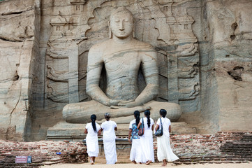Five religious women are standing and admiring the great Samadhi Statue in Polonnaruwa, Sri Lanka.
