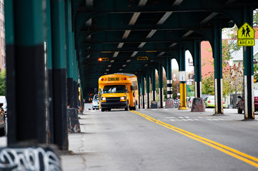 A school bus is passing under the railway bridge in the Bronx, New York city, USA.