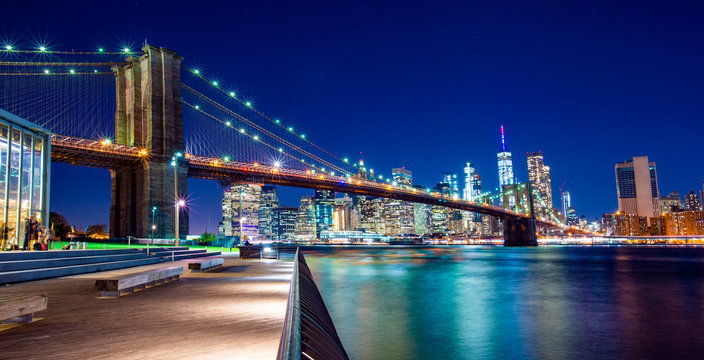 Beautiful Brooklyn Bridge and the illuminated Skyline of Manhattan in the evening with blue sky and smooth water surface. Picture taken from the Brooklyn district, New York, USA.