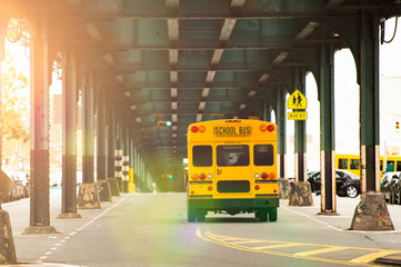 A school bus is passing under the railway bridge in the Bronx, New York city, USA. - obrazy, fototapety, plakaty