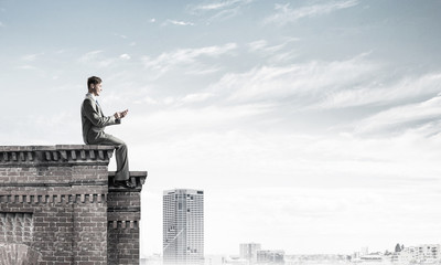 Man on roof edge send message with smartphone and cityscape at b