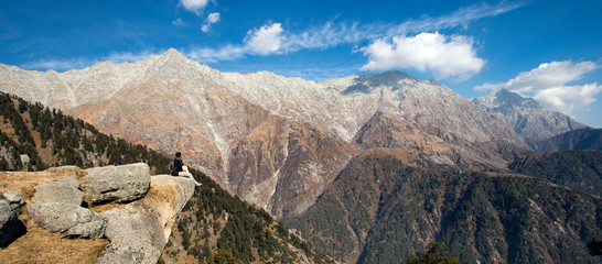 A tourist is enjoying the beautiful view of Dhauladhar Mountain ranges during a sunny day. Triund, Dharamsala, Himachal Pradesh, India.