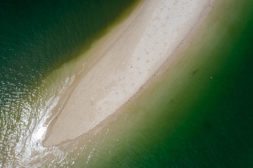 Aerial drone view of a tiny sandy spit surrounded by a green, warm tropical ocean