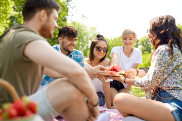 friendship, leisure and food concept - group of happy friends sharing watermelon at picnic in summer park
