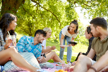 friendship and leisure concept - group of happy friends with non alcoholic drinks and food at picnic in summer park