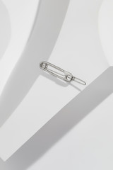 Close up top view of a delicate silver barrette with safety pin-shaped charm, isolated on the white geometric patterned background. Trendy fashion accessories. Minimalist style women's jewellery.