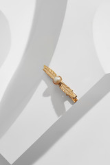 Close up top view of a golden leaf-shaped barrette with pearl bead centerpiece, isolated on the white geometric-patterned background. Trendy fashion accessories. Minimalist style women's jewellery.