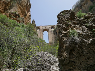 Fototapeta na wymiar Old bridge connecting two parts of a city over a canyon in the mountains of Ronda, Spain, seen from below