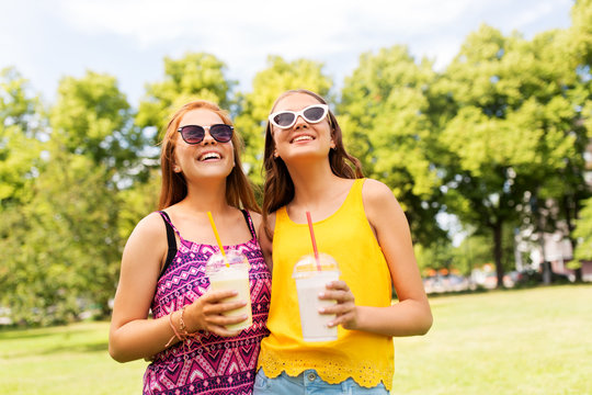 leisure and friendship concept - happy smiling teenage girls or friends with milk shakes or smoothie drinks at summer summer park