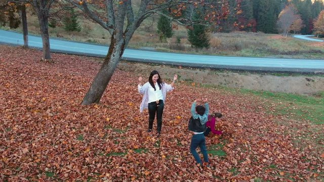 Mom and her children have fun in the autumn forest. They jump and throw leaves into the air. They are laughing. The family is happy. Slow motion. Shooting from the quadcopter.