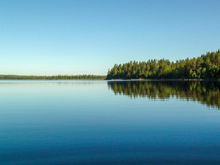 Blue lake as a mirror for green forest and blue sky