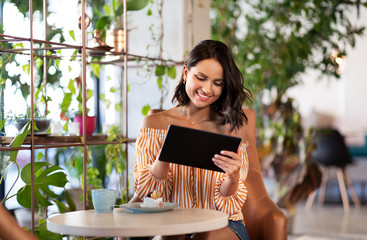 technology and people concept - happy woman with tablet pc computer and cake at cafe or coffee shop