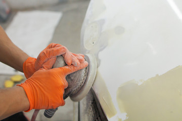 men's hands in orange gloves polish the hood of a car with a pneumatic polisher in the garage