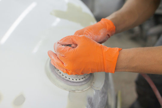 men's hands in orange gloves polish the hood of a car with a pneumatic polisher in the garage