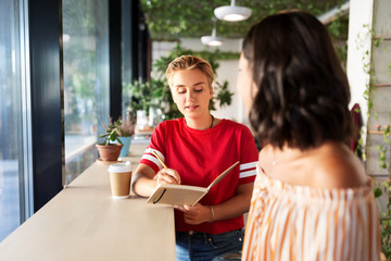 people and friendship concept - young woman with friend at cafe writing to notebook
