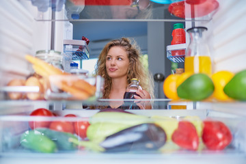 Woman standing in front of fridge full of groceries and looking for something to eat. Picture taken...