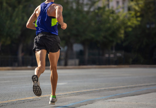 Running in the city roads. Young man runner, back view, blur background
