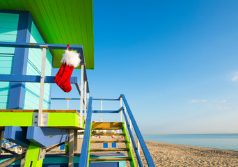 Santa stocking Christmas decoration hanging from brightly colored lifeguard tower next to calm tropical seas in Miami Beach, Florida, USA