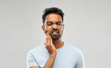 people, dentistry and health problem concept - indian man suffering from toothache over grey...