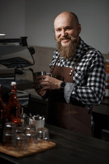 Brutal young barista in an apron makes coffee at the bar in a modern cafe