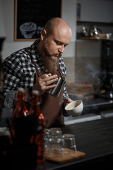 Brutal young barista in an apron makes coffee at the bar in a modern cafe