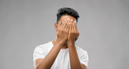 emotion, expression and people concept - scared man covering his face with hands over grey...